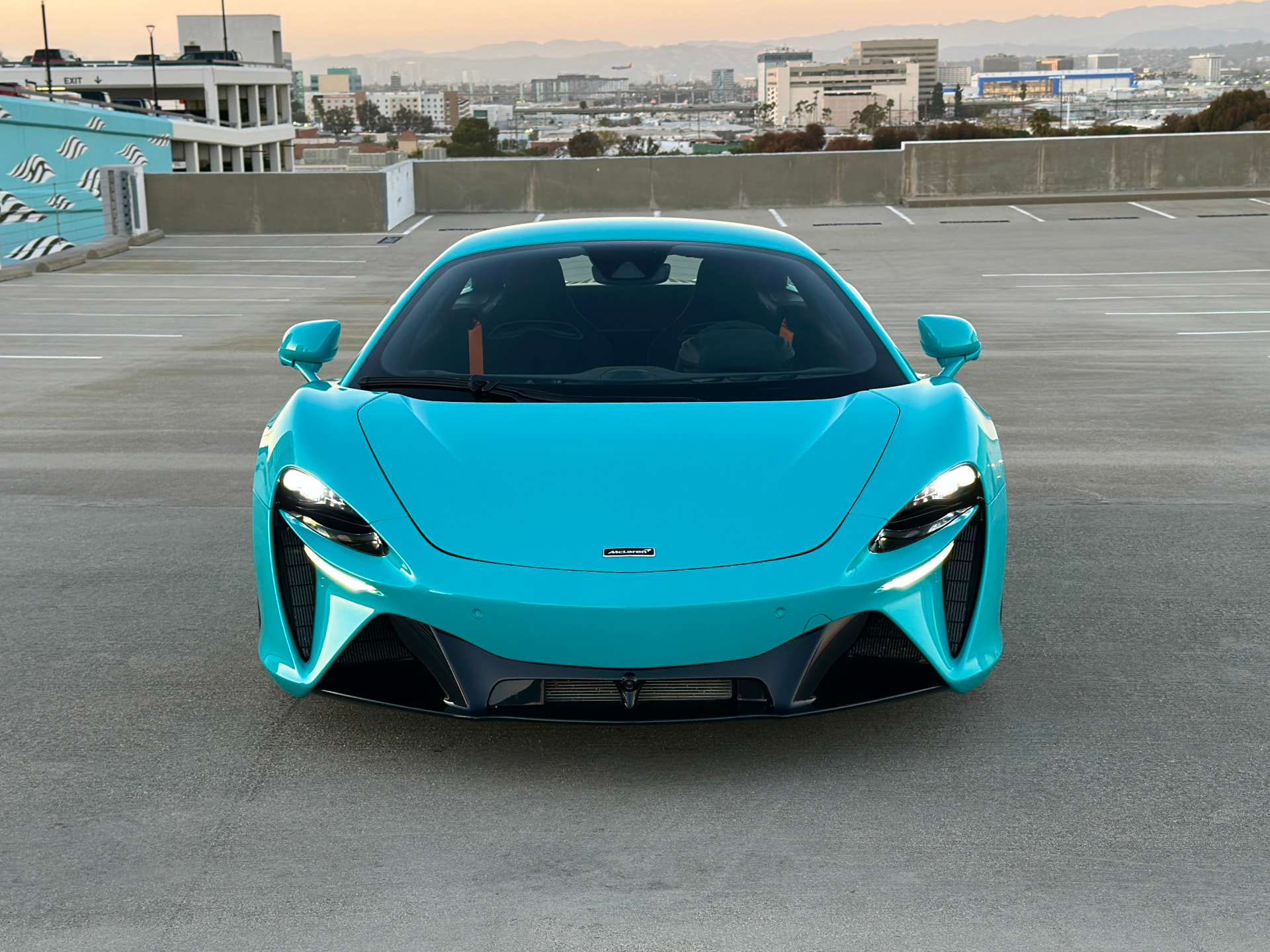 Turquoise McLaren viewed head-on on a rooftop parking deck with the Los Angeles skyline behind it