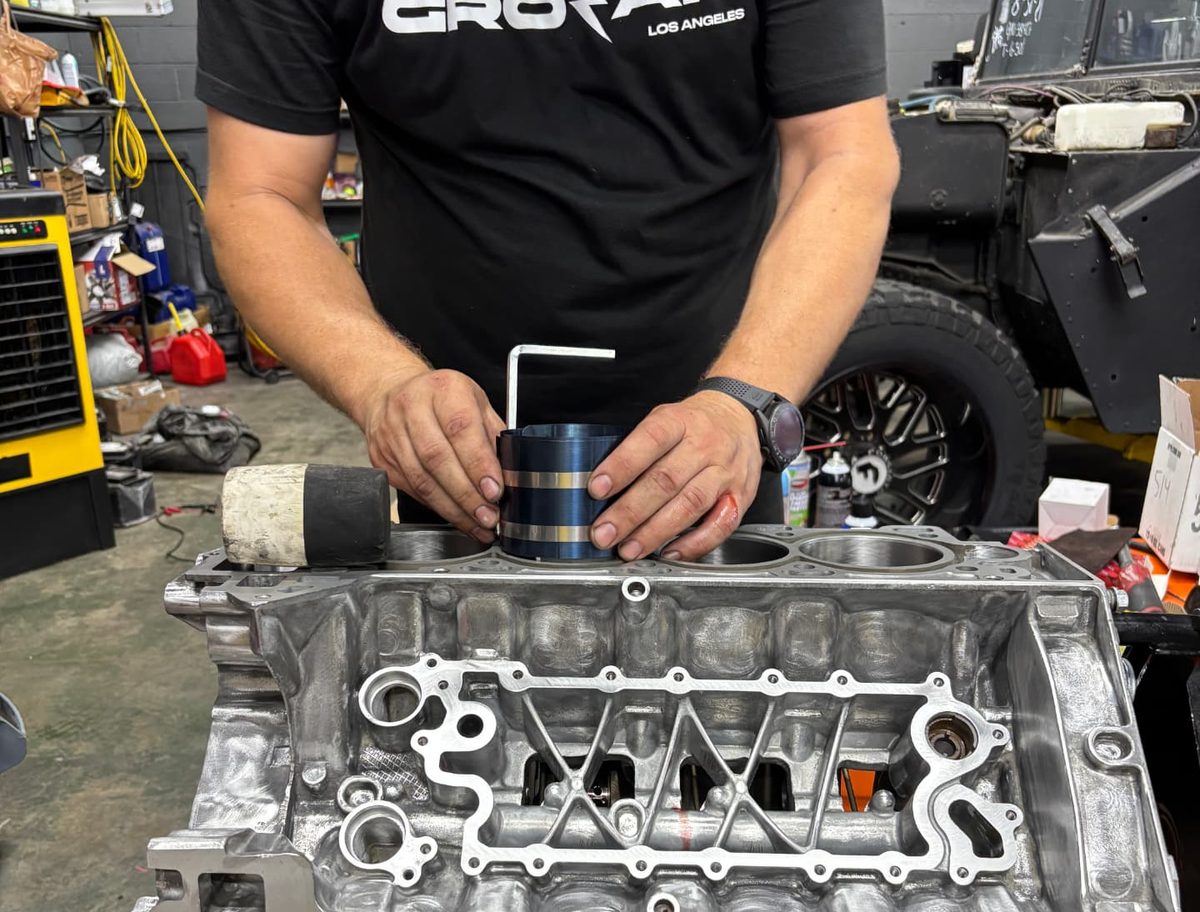 A technician fitting a piston ring compressor to a stripped engine block in the workshop